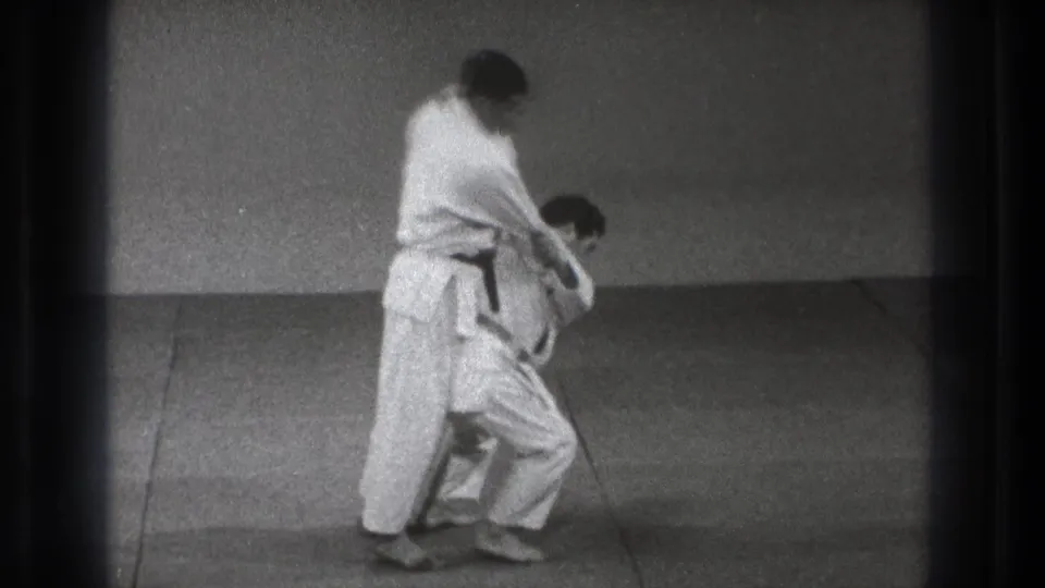 The standing practitioner in a black belt begins lifting his partner during the Tokyo 1971 karate demonstration.