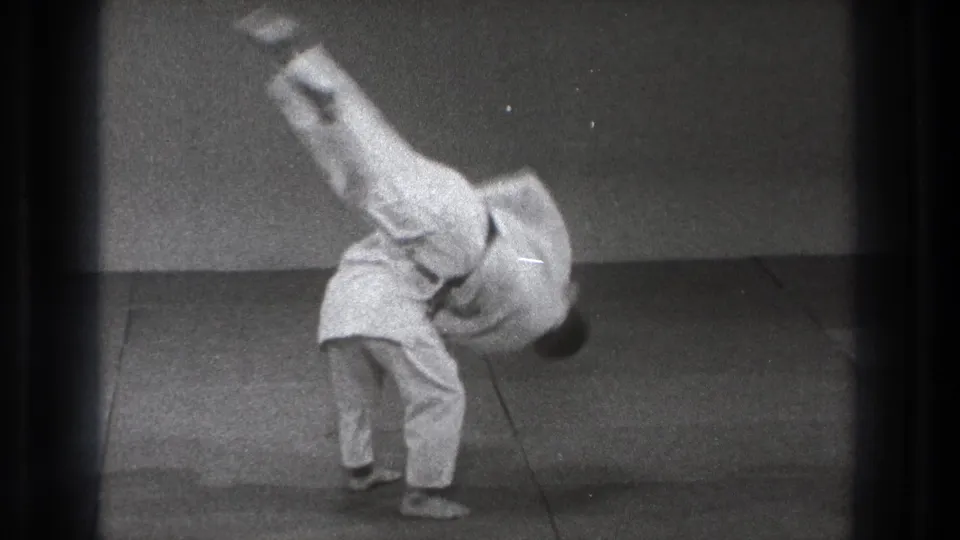 The black-and-white 8mm frame shows the partner still inverted over the mat during the karate throw in Tokyo, 1971.