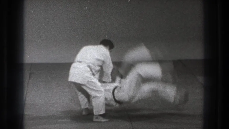 In 1971 Tokyo footage, one karate practitioner throws another during an indoor demonstration on a tatami mat.