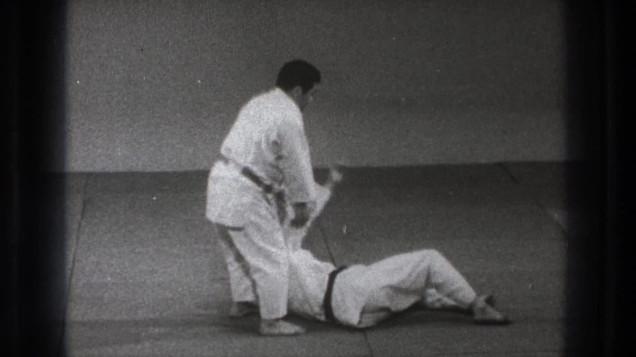 During the Tokyo karate demonstration, one practitioner stands over a partner who has landed on the mat after a throw.