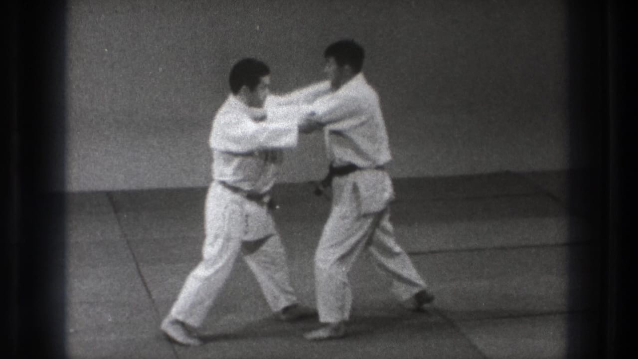 Two judo practitioners in white uniforms make upper-body contact during a controlled technique in Tokyo.