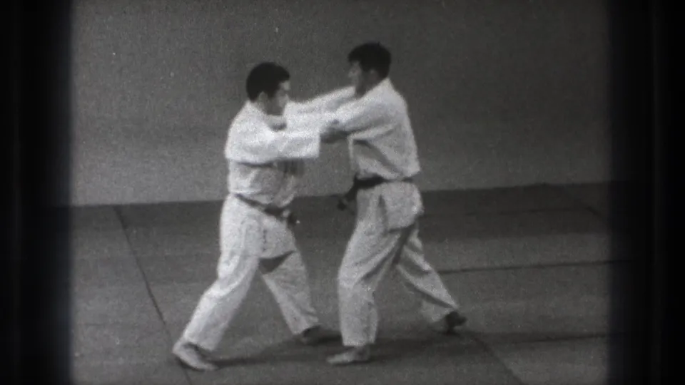 Two judo practitioners in white uniforms make upper-body contact during a controlled technique in Tokyo.