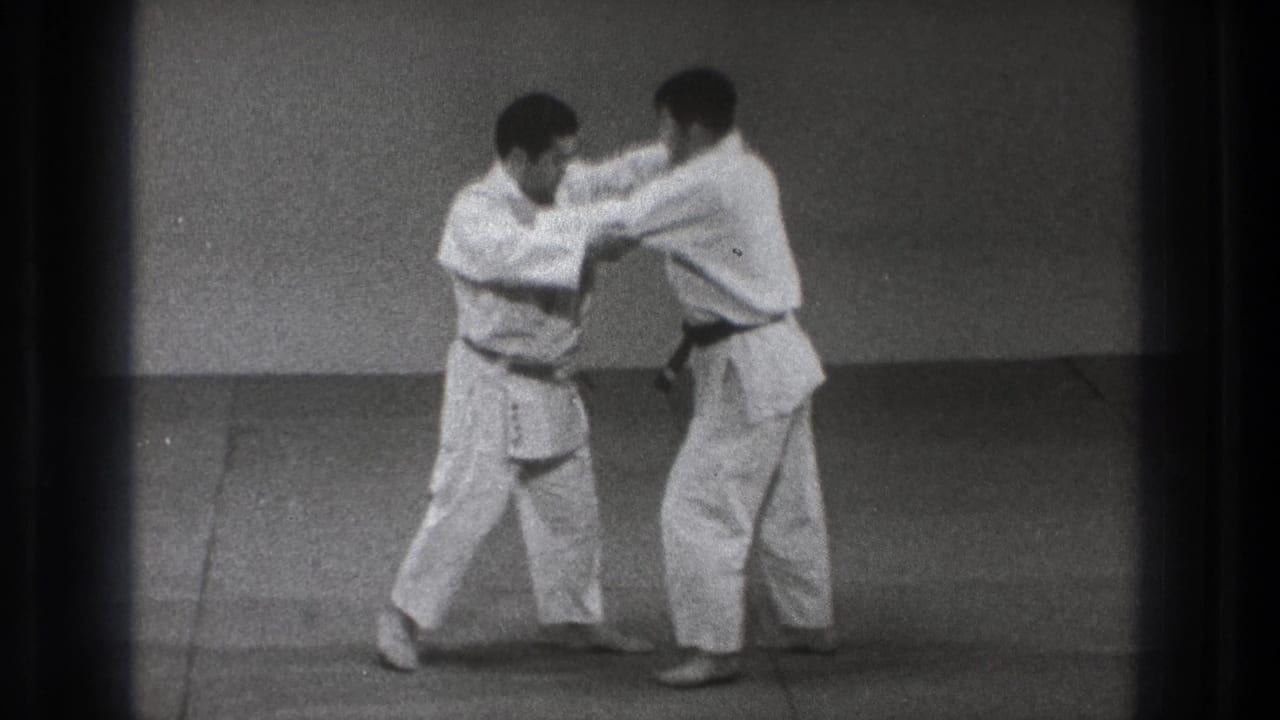 Two adult men in white martial-arts uniforms step in unison while maintaining arm grips during the 1971 Tokyo practice scene.