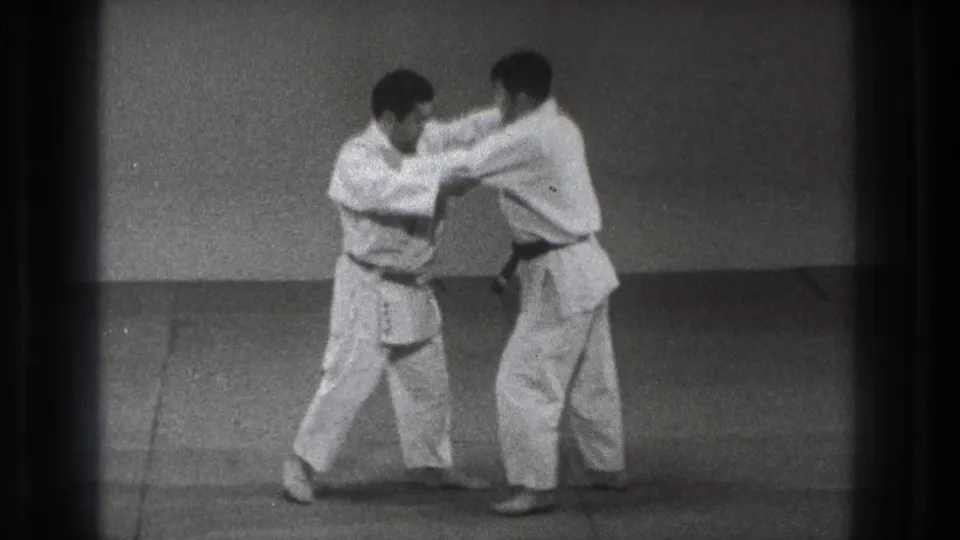 Two adult men in white martial-arts uniforms step in unison while maintaining arm grips during the 1971 Tokyo practice scene.