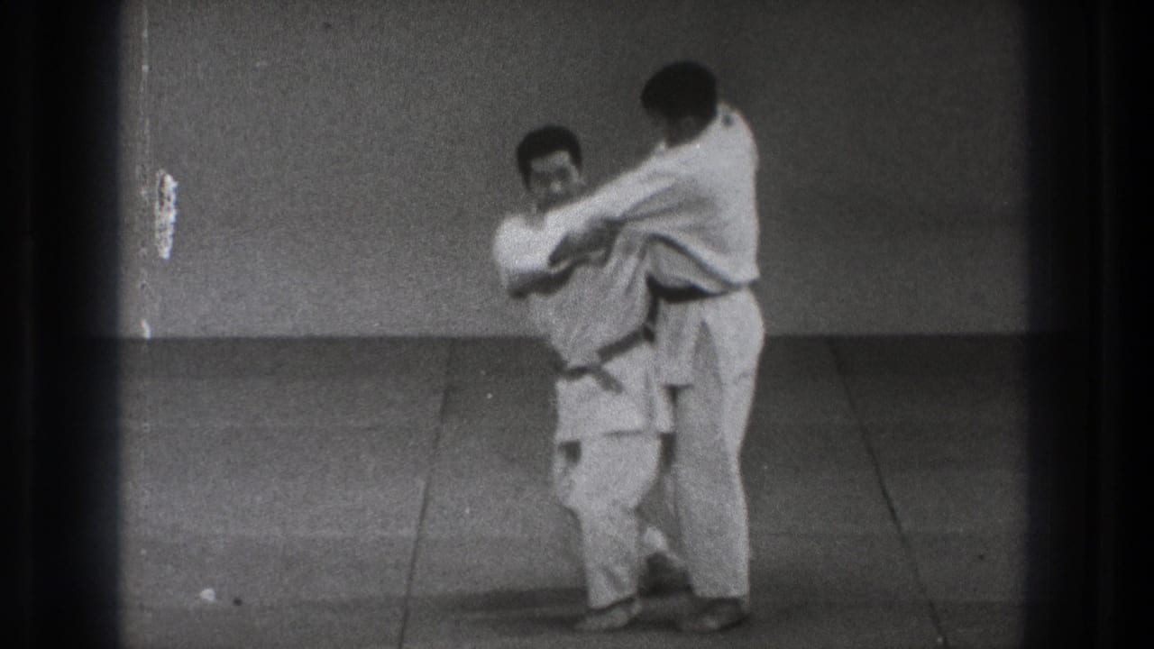 One uniformed man turns into the hold as his partner stays close behind during a grappling technique in metadata-supported 1971 Tokyo.