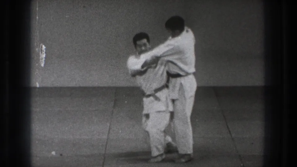 One uniformed man turns into the hold as his partner stays close behind during a grappling technique in metadata-supported 1971 Tokyo.
