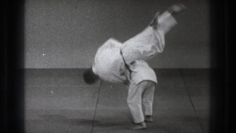 A man in a white judogi is airborne over his partner during a slow-motion judo throw in Tokyo, 1971.