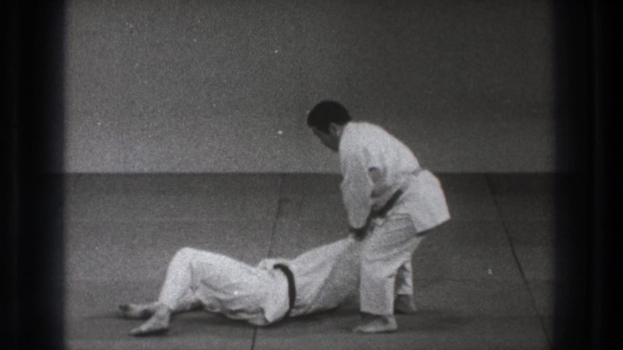 After the throw, one man lies on the grey mat as the standing practitioner keeps hold of his arm in the Tokyo dojo scene.