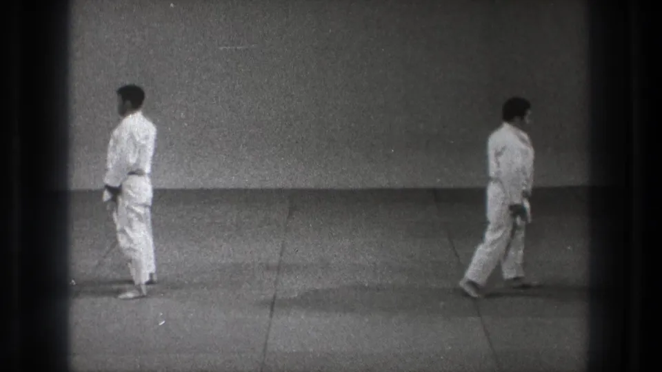 In supported 1971 Tokyo footage, a man in a white gi stands on a simple mat as the 8mm frame edge remains visible.