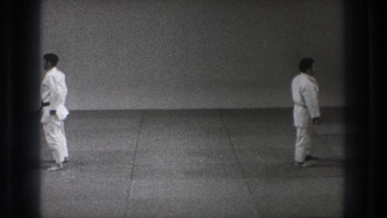 Two men in white gi appear across a simple mat in the 1971 Tokyo martial arts footage, framed by dark 8mm borders.