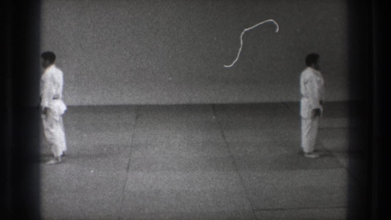 The 8mm frame shows two martial arts practitioners in white gi positioned apart on a plain mat in supported 1971 Tokyo footage.