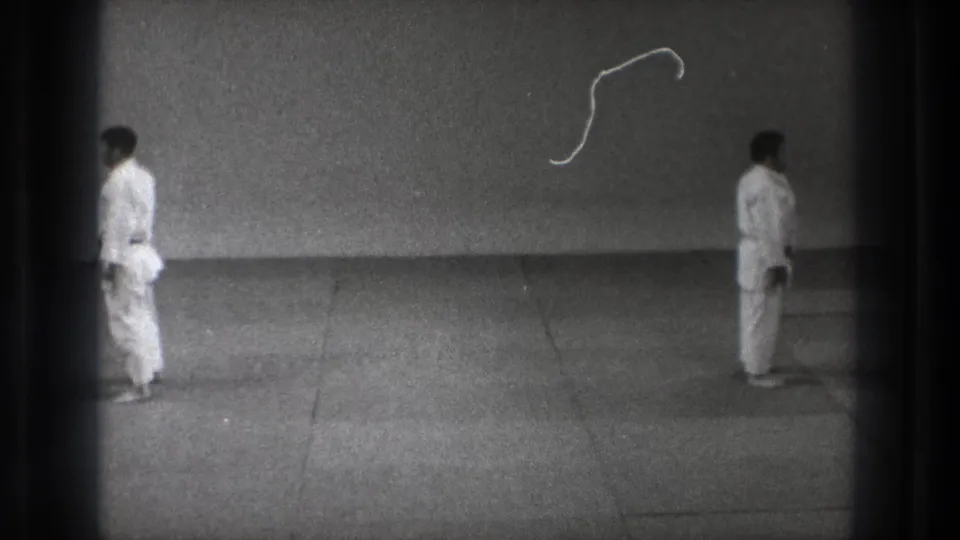 The 8mm frame shows two martial arts practitioners in white gi positioned apart on a plain mat in supported 1971 Tokyo footage.