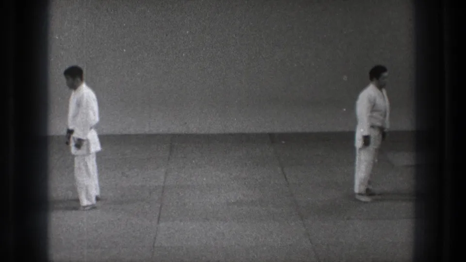 Two judo practitioners in white uniforms face inward on a plain mat in 1971 Tokyo footage.