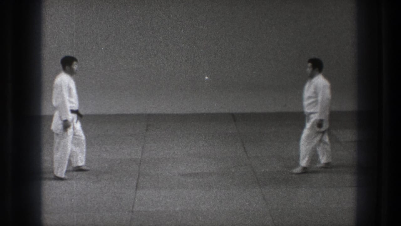 Two judo practitioners in white judogi walk toward each other in a black-and-white 8mm frame.