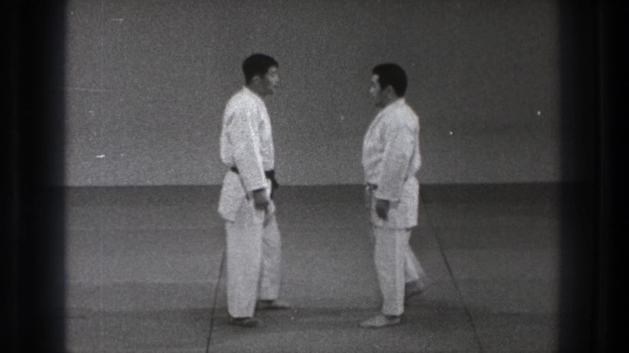 In 1971 Tokyo footage, two adult men in white gi stand facing each other on tatami-style mats before beginning a martial arts technique.