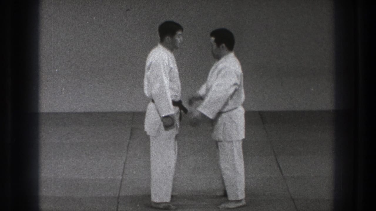 Two men in gi stand close together as one begins a hand movement near the other's arm.