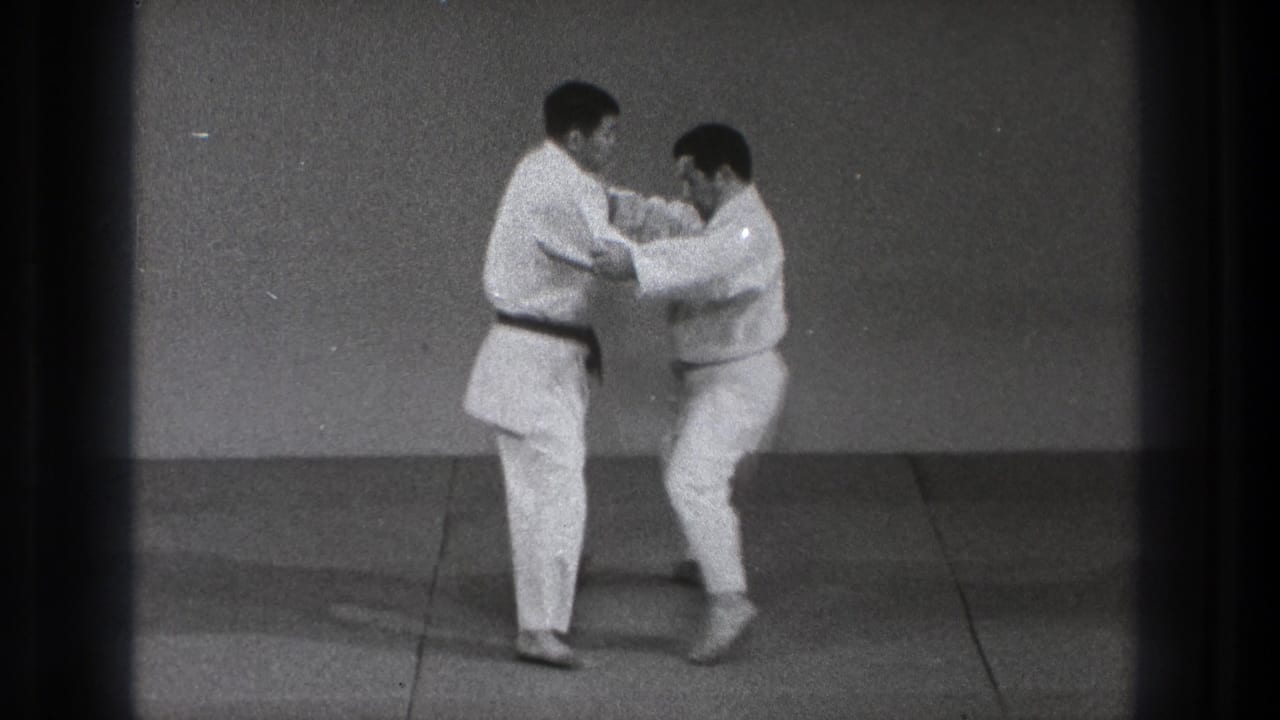 The martial arts demonstration continues as one practitioner steps in and both maintain arm contact on the dojo mat in 1971 Tokyo footage.