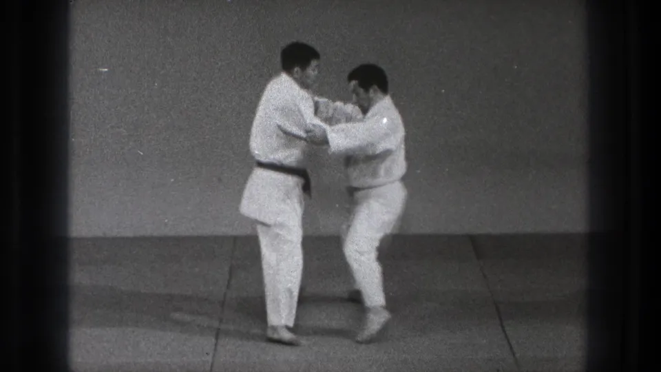 The martial arts demonstration continues as one practitioner steps in and both maintain arm contact on the dojo mat in 1971 Tokyo footage.