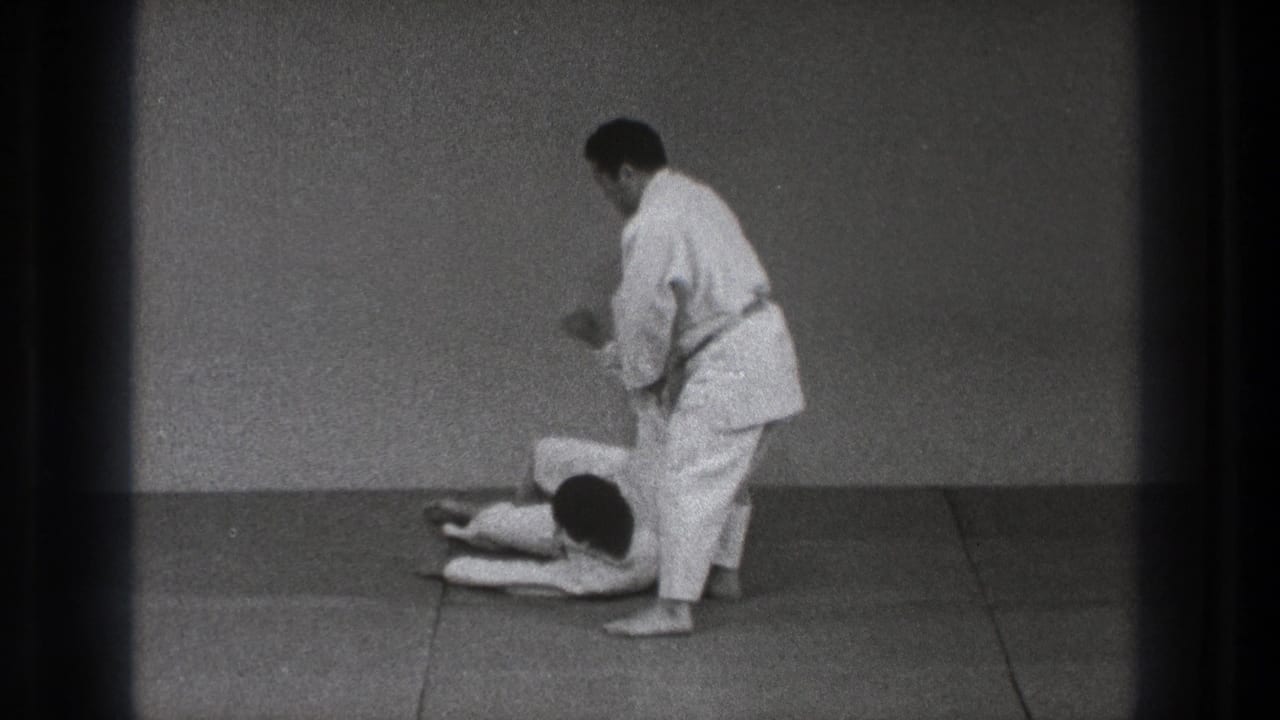 After the throw, one adult practitioner lies on the dojo mat while the other remains standing nearby in Tokyo 1971 footage.