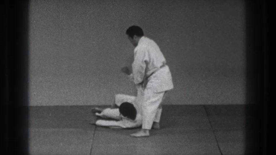 After the throw, one adult practitioner lies on the dojo mat while the other remains standing nearby in Tokyo 1971 footage.