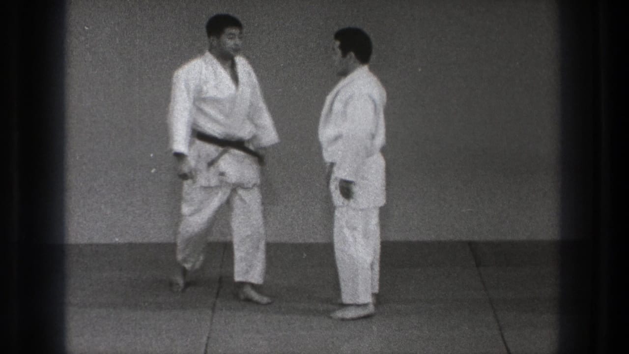 In 1971 Tokyo footage, two adult men in white judo gis face each other on a training mat, one wearing a black belt.