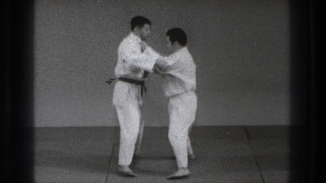 The men begin a controlled grappling movement, holding each other's gis while standing on the training mat.