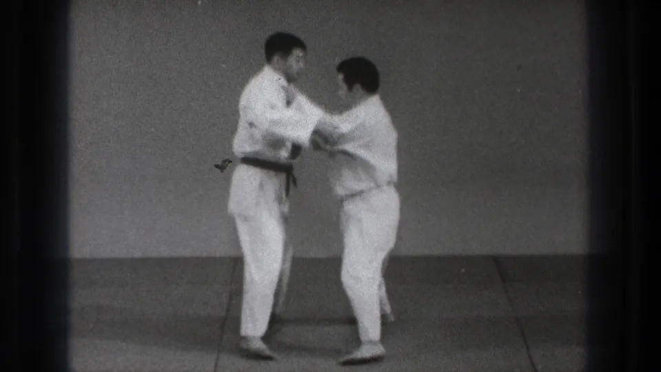 The men begin a controlled grappling movement, holding each other's gis while standing on the training mat.