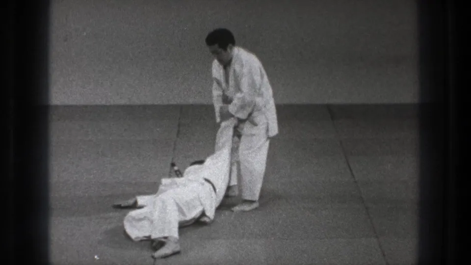During the Tokyo 1971 judo practice sequence, one man is down on the mat as the standing partner controls his leg.