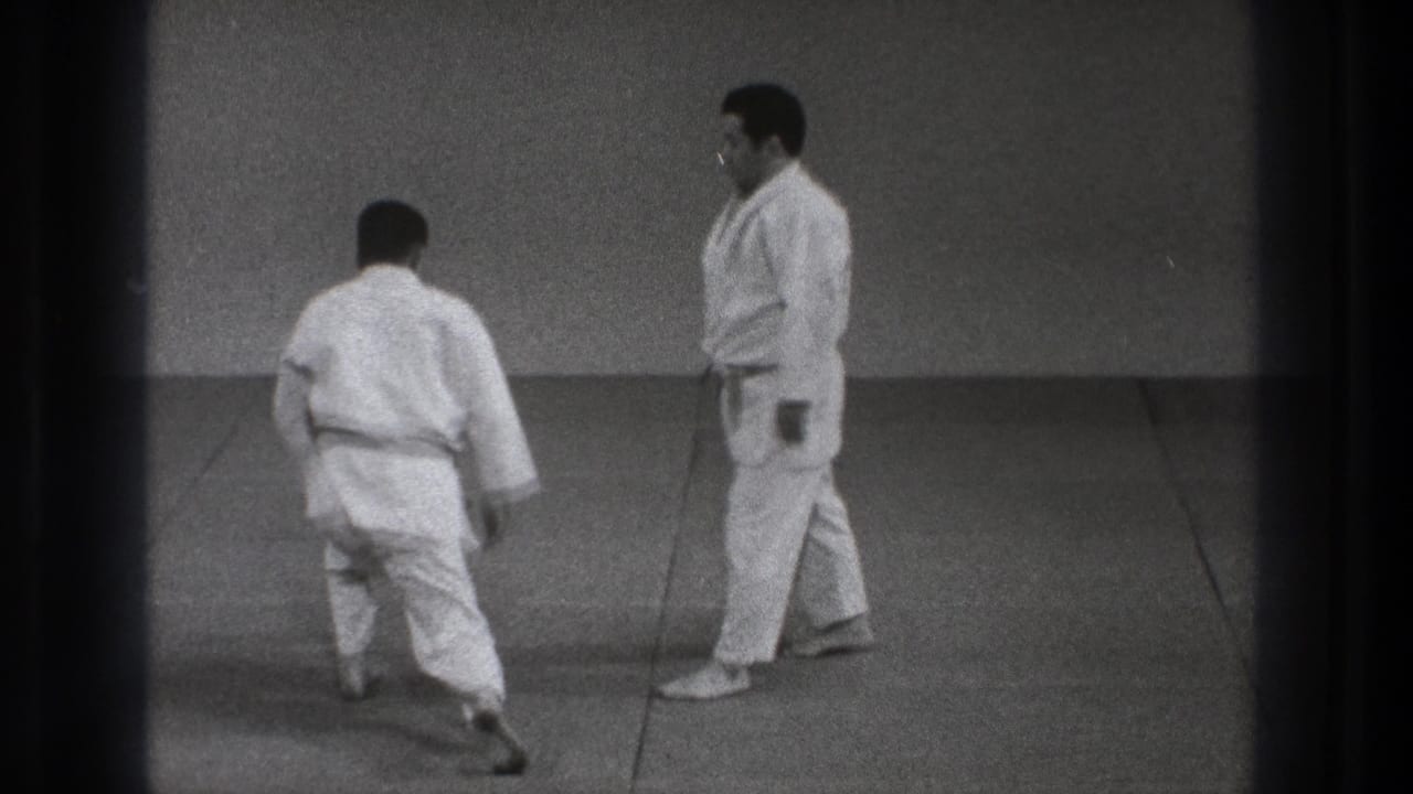 Two men in white judo uniforms move on a mat, one partly turned away.