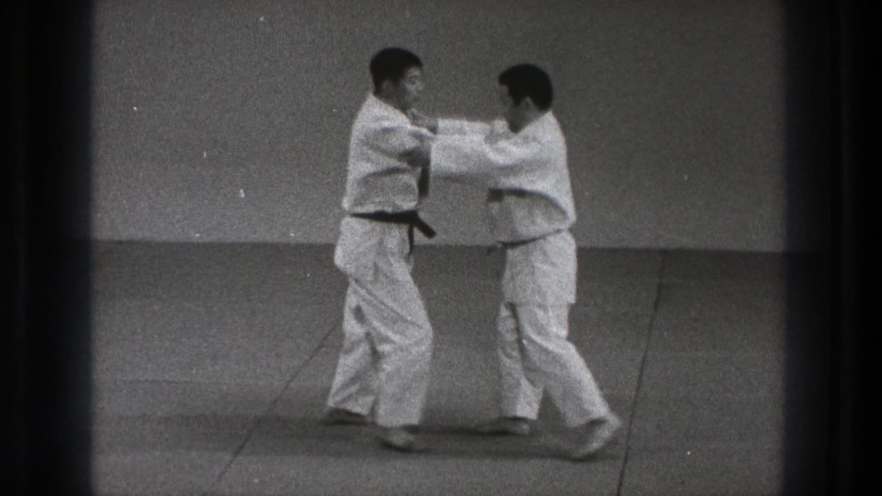 Two judo practitioners in white uniforms begin a standing grip on the mat, with rank belts visible.