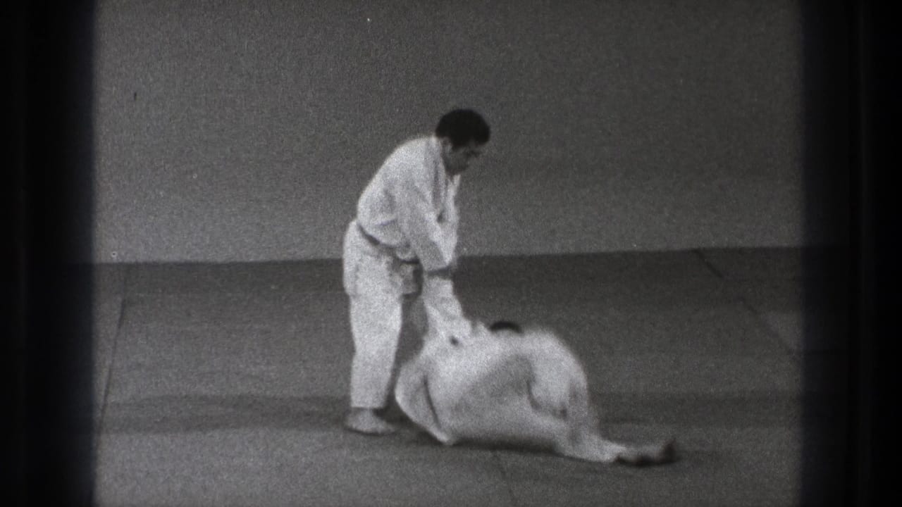 During the 1971 demonstration, one practitioner goes down toward the mat as the standing man maintains arm control.