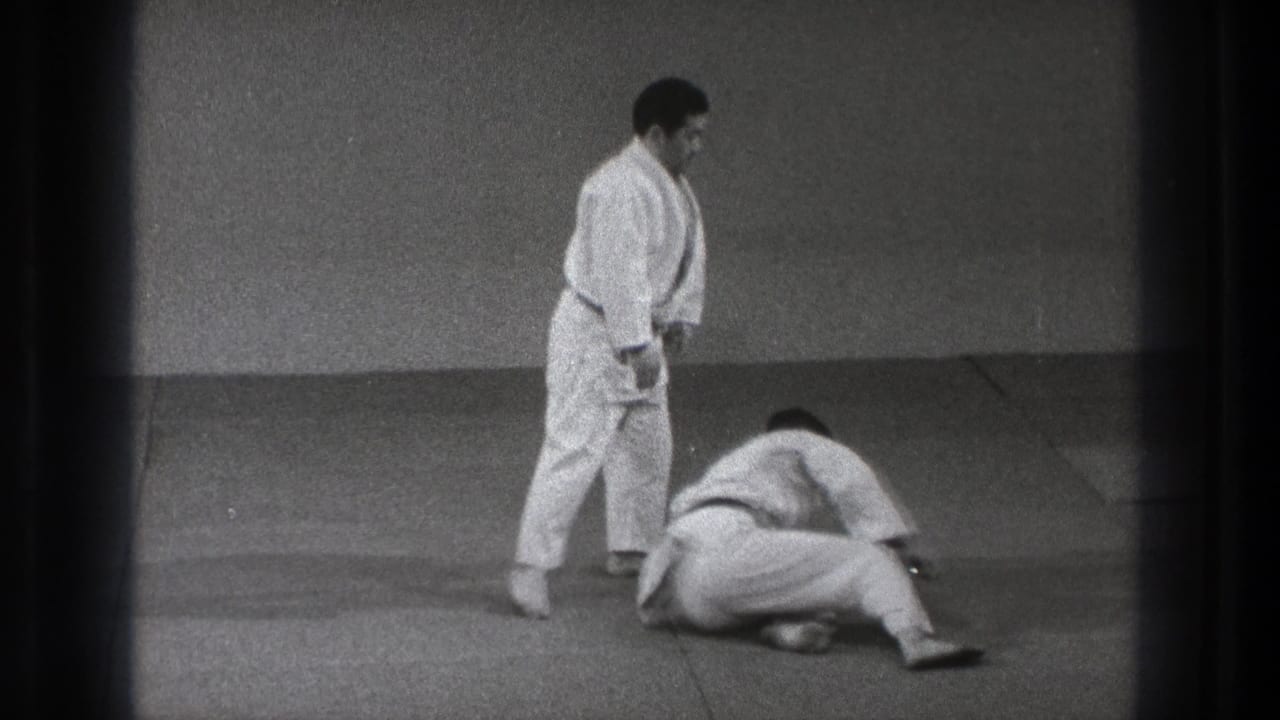Two men in white gi on mats, one standing while the other is down after a throw.