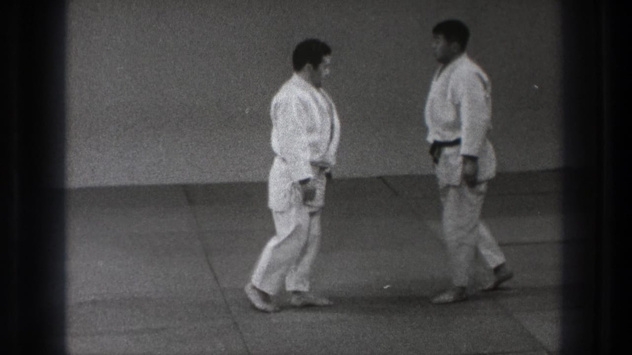 Two adult martial arts practitioners in white gi face each other on mats in the supplied 1971 Tokyo footage.