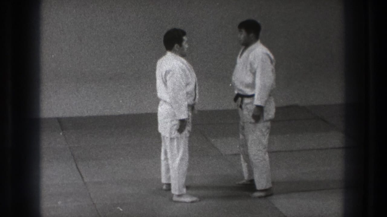 In Tokyo, Japan in 1971, two adult men in white judo gis and dark belts stand facing each other on tatami mats.