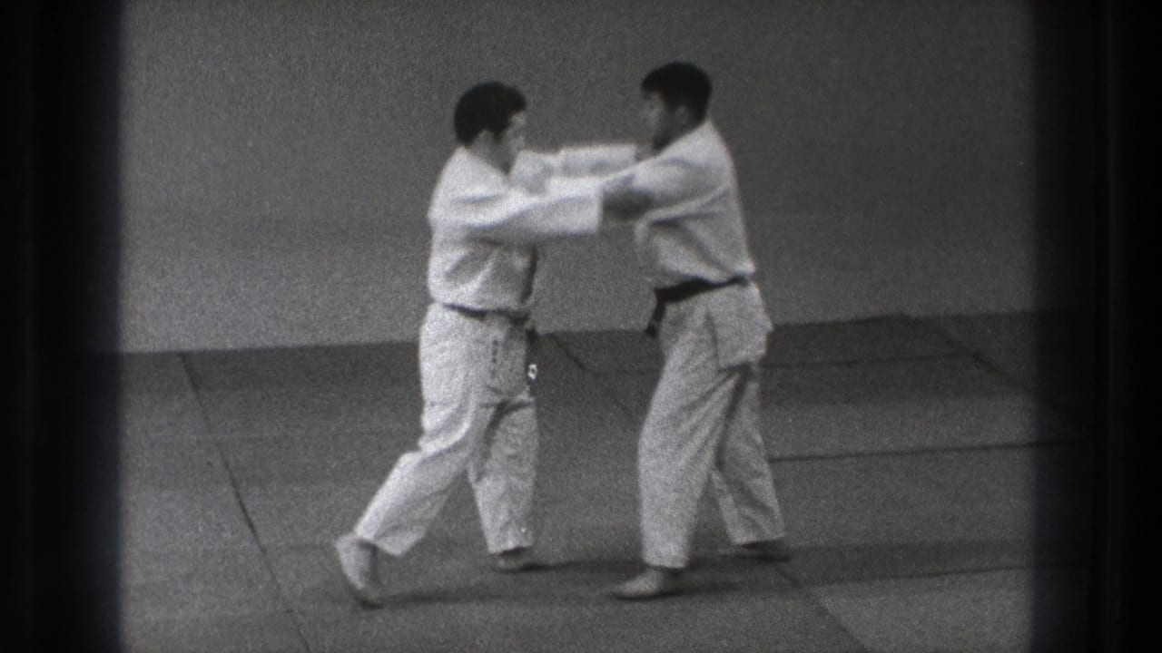 Two adult men in judo gis make sleeve and lapel contact on tatami mats during a 1971 Tokyo practice exchange.