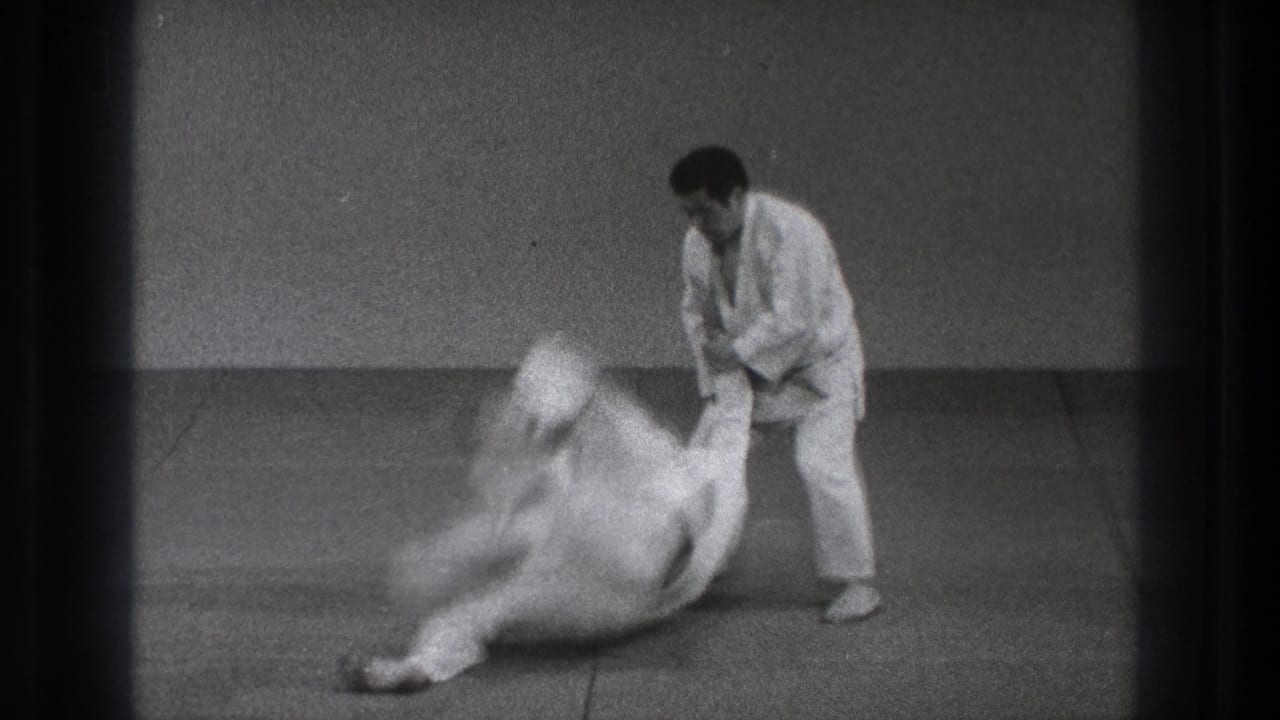 Two men in white judogi on tatami as one begins throwing the other.