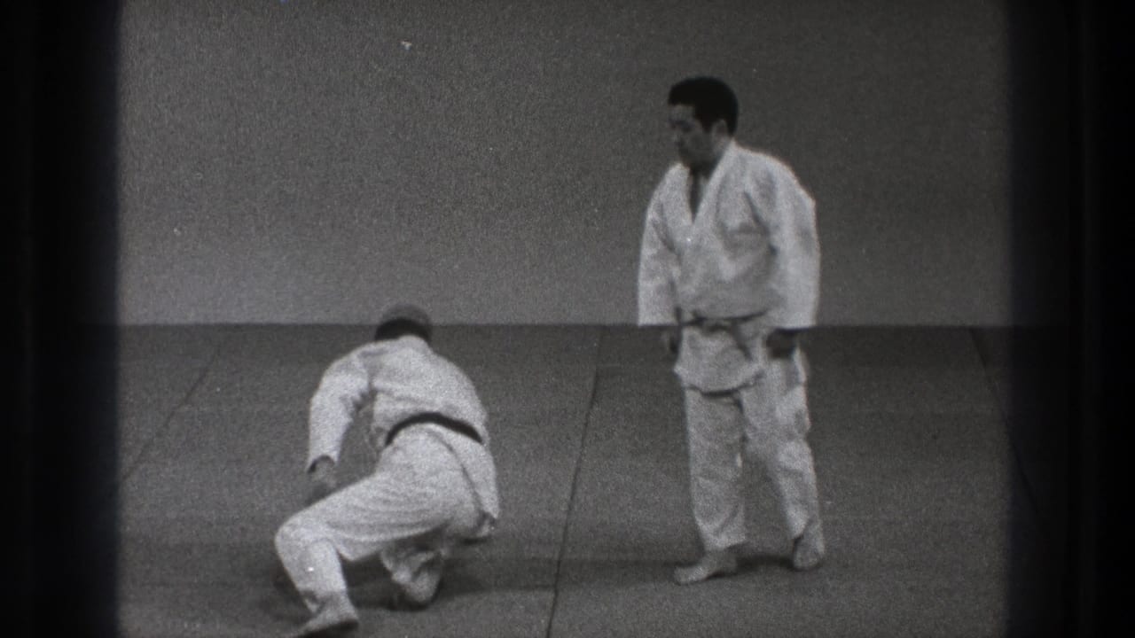 1971 Tokyo judo practice frame showing one adult practitioner kneeling after the throw while the black-belt partner stands on the tatami.