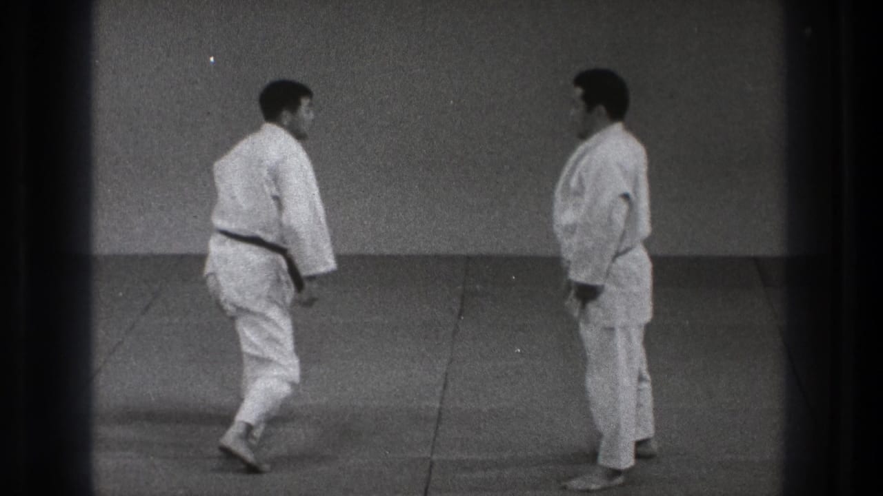 1971 Tokyo judo practice frame with two adult men in white judogi facing each other during a reset on the dojo mat.