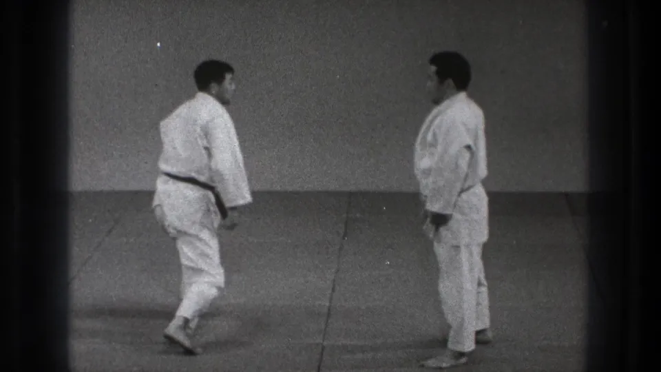 1971 Tokyo judo practice frame with two adult men in white judogi facing each other during a reset on the dojo mat.