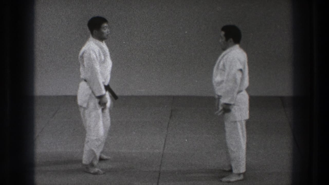 In 1971 Tokyo footage, two adult men in white karate gi face one another on a dojo mat before beginning a practice sequence.