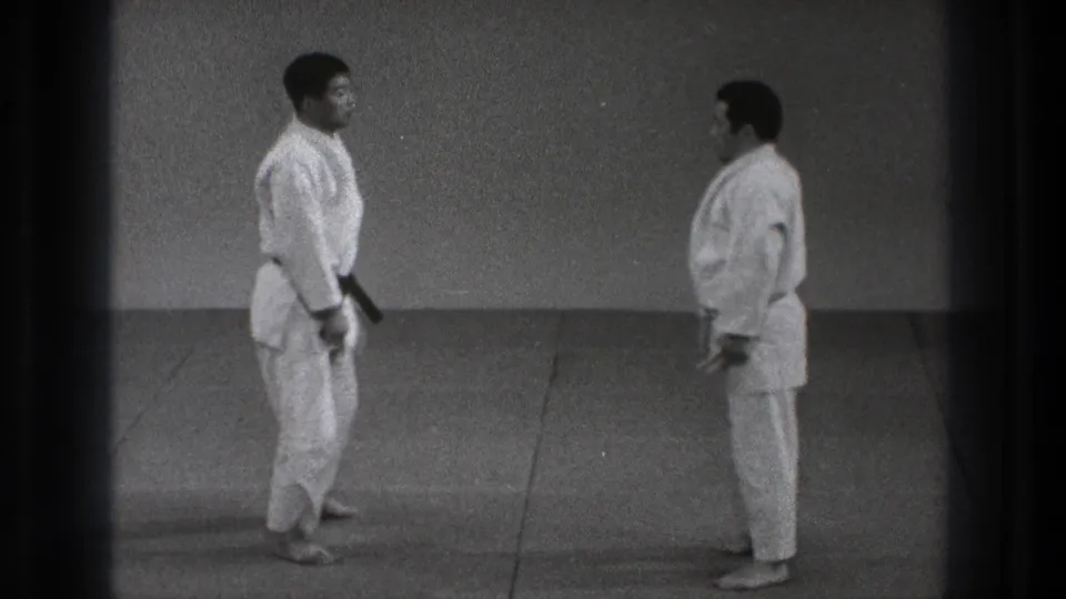 In 1971 Tokyo footage, two adult men in white karate gi face one another on a dojo mat before beginning a practice sequence.