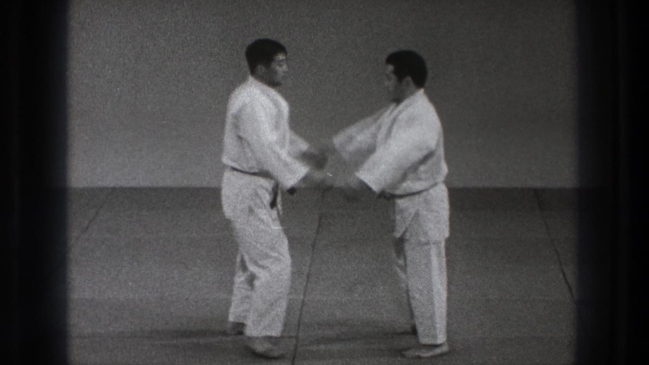 The karate partners make hand contact on the mat, beginning a slow defensive movement in the 1971 Tokyo dojo footage.