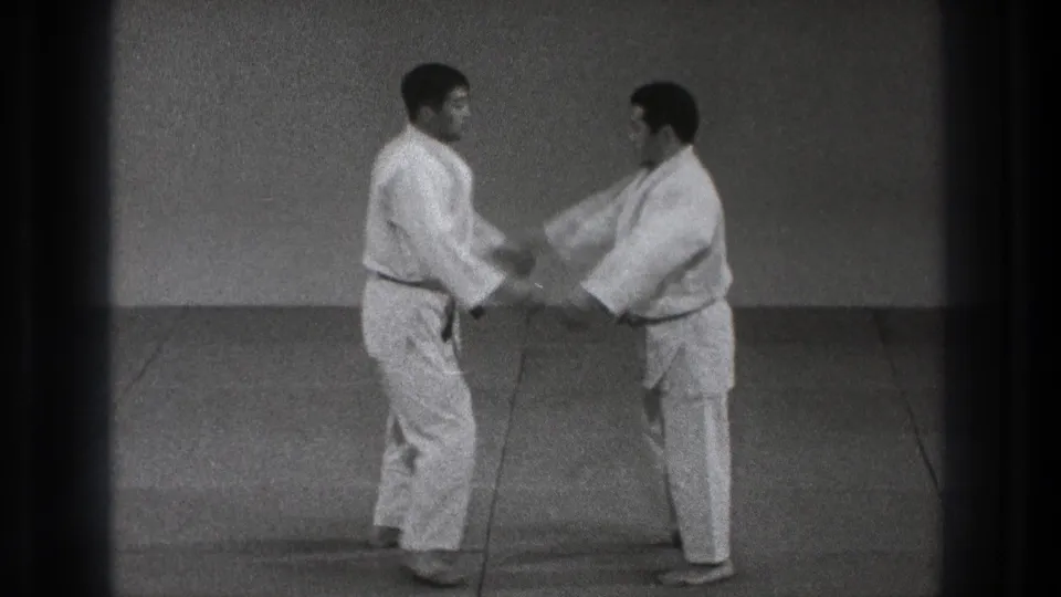 The karate partners make hand contact on the mat, beginning a slow defensive movement in the 1971 Tokyo dojo footage.
