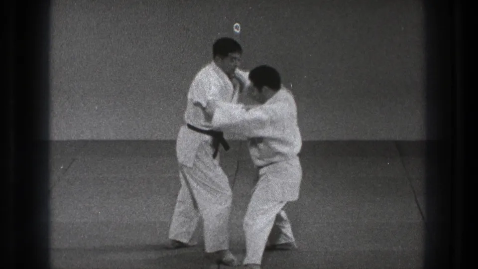 The partners move into close-range contact, with one turning into the other during the controlled karate technique.