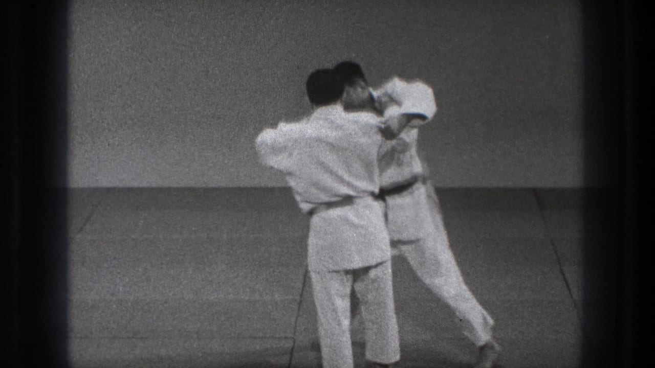 Two martial artists in white gi grip each other while standing on a mat.