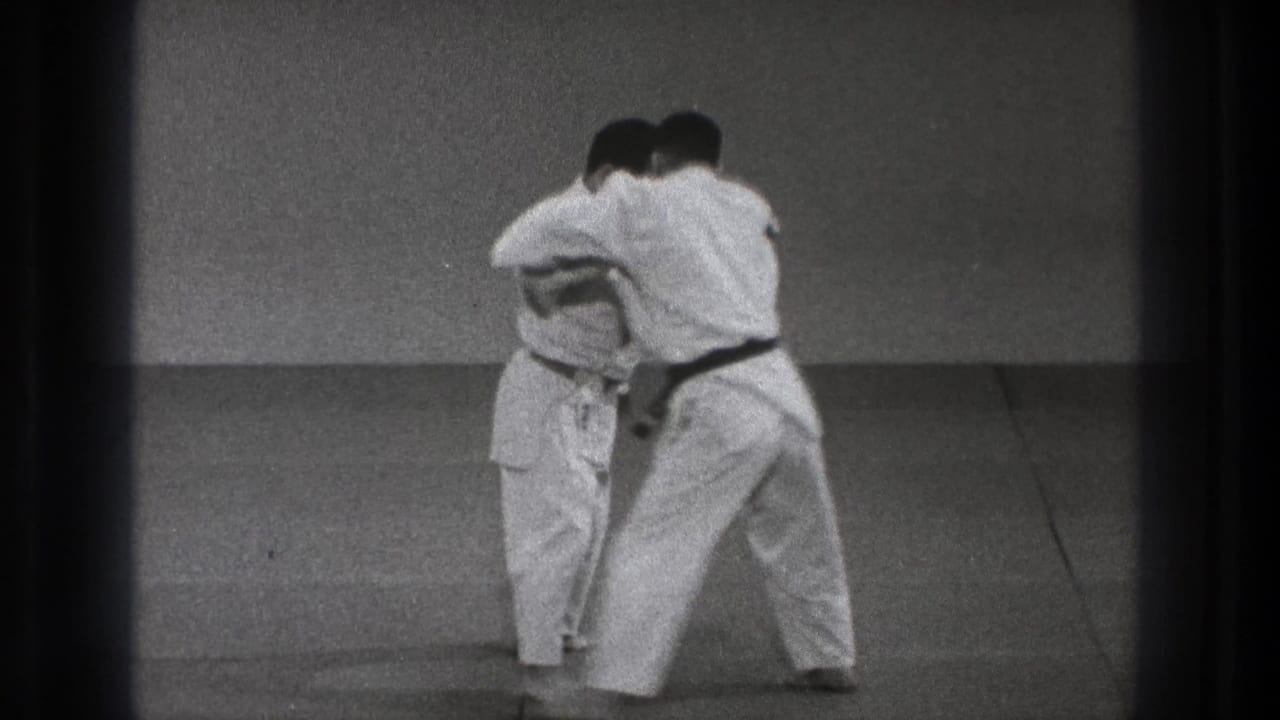 Two adult martial artists in white gi work from a close standing hold during the Tokyo judo demonstration.