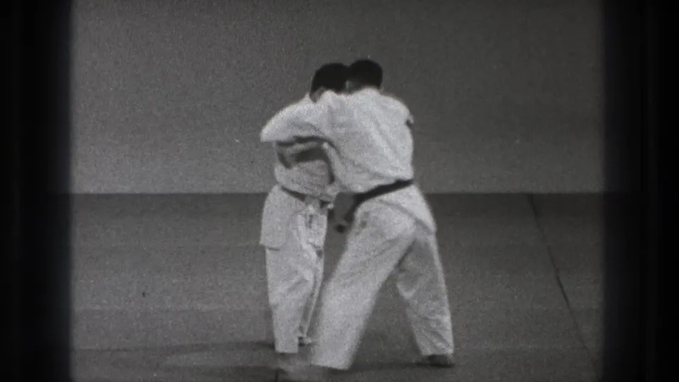 Two adult martial artists in white gi work from a close standing hold during the Tokyo judo demonstration.