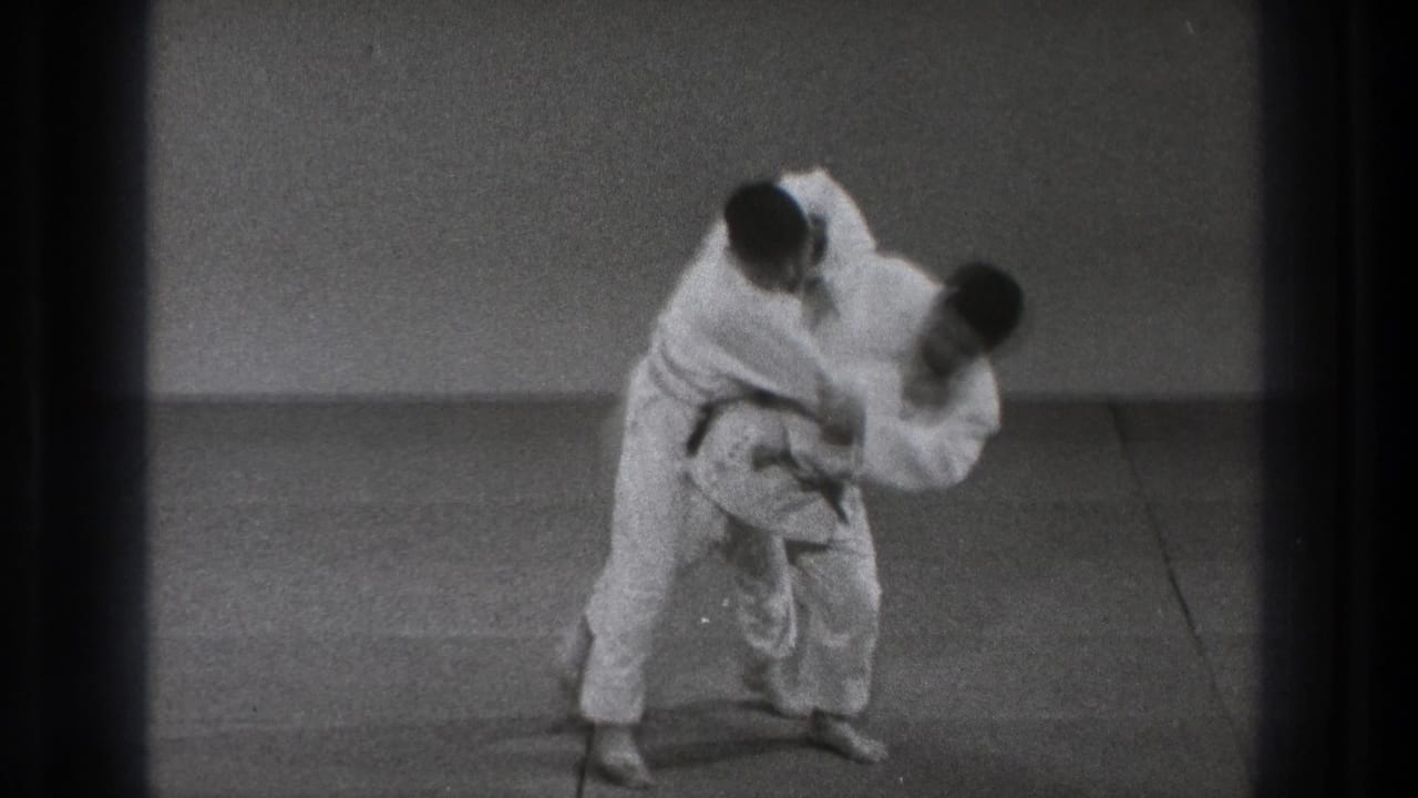 A judo practitioner in a white gi appears to load and lift his partner into a throwing motion on the mat.