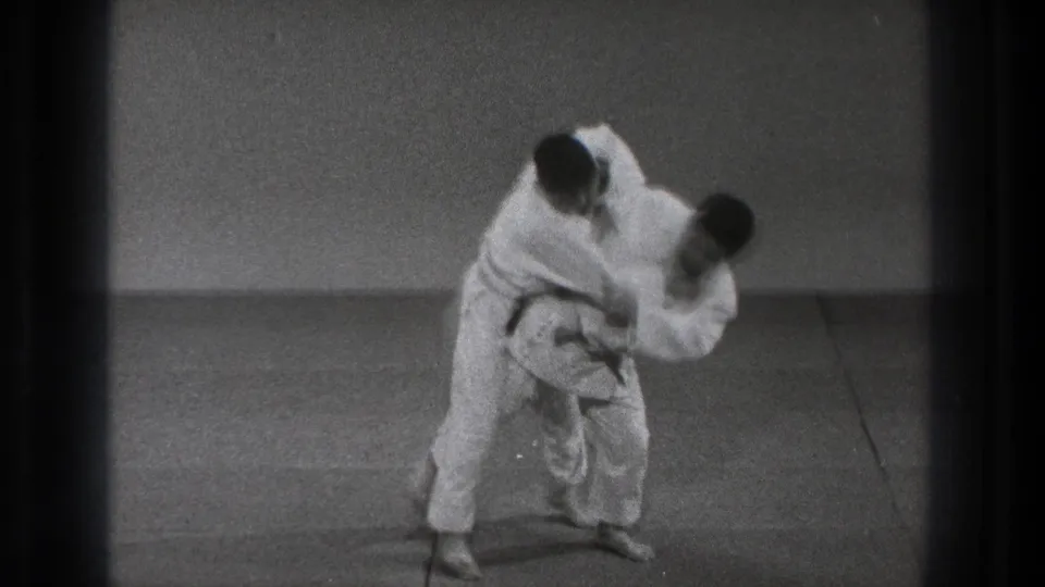 A judo practitioner in a white gi appears to load and lift his partner into a throwing motion on the mat.