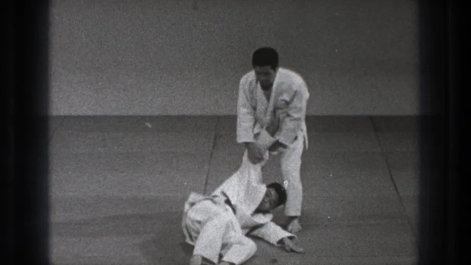 At the end of the technique, one adult practitioner stands over his partner, who is down on the practice mat.
